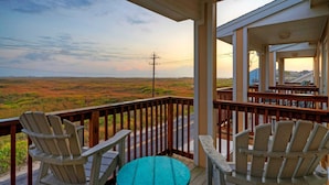 A balcony with Adirondack chairs and a small table, overlooking a scenic landscape with a road and power lines. - The Beautiful Place by Avantstay Mins to Beach + Family-friendly Pool (Corpus Christi)