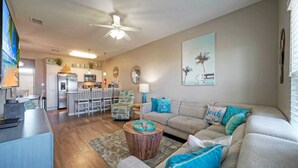 A living room with a sofa, coffee table, and a kitchen in the background. - The Beautiful Place by Avantstay Mins to Beach + Family-friendly Pool (Corpus Christi)