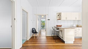 Une cuisine moderne avec des meubles blancs, un plancher en bois et un petit îlot central doté de tabourets de bar.