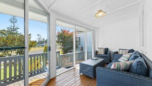 Un balcon extérieur abrité, doté de meubles en osier et offrant une vue sur la rue et les arbres.