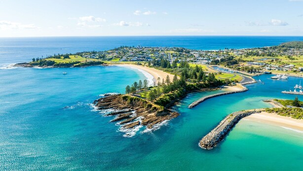 Vue aérienne d’une ville côtière avec une plage, un port de plaisance et des quartiers résidentiels.