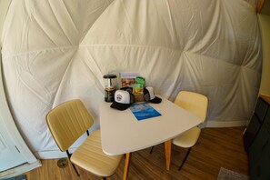 Une petite pièce avec une table blanche, deux chaises, une lampe, un livre et un sac de collations.