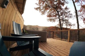 Une terrasse en bois avec des sièges extérieurs, offrant une vue sur un paysage vallonné aux couleurs automnales.