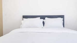 Un lit avec une literie blanche et une tête de lit sombre.