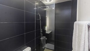 Une salle de bain moderne avec des carreaux foncés, une douche en verre, des toilettes et une serviette accrochée au mur.
