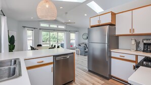 A modern kitchen with a dishwasher, refrigerator, and wooden cabinets. - Dunes & Waves Retreat -  Perfect Lake Getaway (Mears)