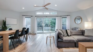 A spacious living area with a wooden dining table, black chairs, a grey sofa, and a ceiling fan. - Dunes & Waves Retreat -  Perfect Lake Getaway (Mears)