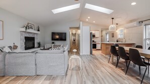 A modern living room with a sectional sofa, a fireplace, and a TV. There is a dining area with a wooden table and chairs. - Dunes & Waves Retreat -  Perfect Lake Getaway (Mears)