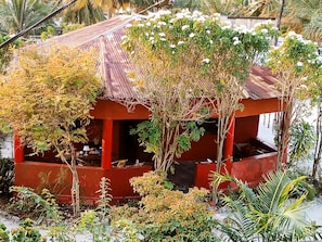 A small, red-roofed structure surrounded by various plants and trees. - Jambiani Holiday Villa (Jambiani)