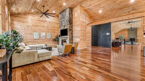 A spacious living area with a stone fireplace, wooden flooring, and a large TV mounted on the wall. - Grand Timber by Avantstay Indoor Pool + Sports Court + Game Room & More! (White Haven)