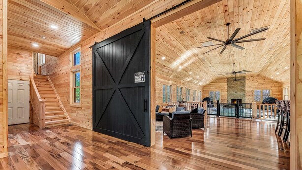 A spacious wooden interior with a large sliding door, a staircase, and a seating area with a fireplace. - Grand Timber by Avantstay Indoor Pool + Sports Court + Game Room & More! (White Haven)