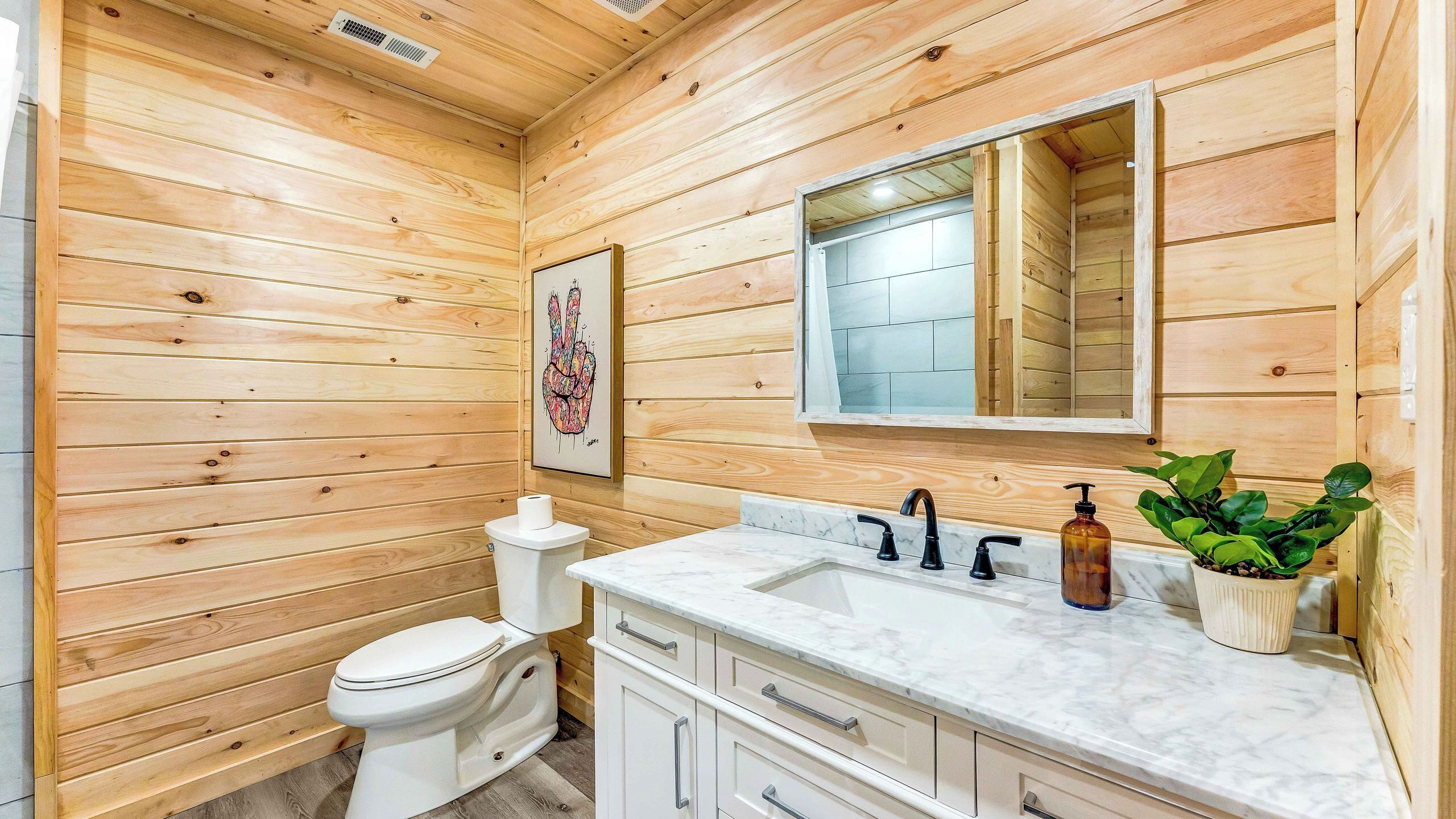 Een badkamer met houten lambrisering, een toilet, wastafel en spiegel.
