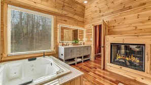 A wooden cabin interior with a large bathtub, a vanity with a mirror, and a fireplace. - Grand Timber by Avantstay Indoor Pool + Sports Court + Game Room & More! (White Haven)