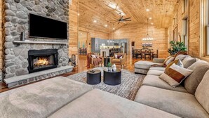 A cozy living room with a stone fireplace, a flat-screen TV, and a modern sofa set. - Grand Timber by Avantstay Indoor Pool + Sports Court + Game Room & More! (White Haven)