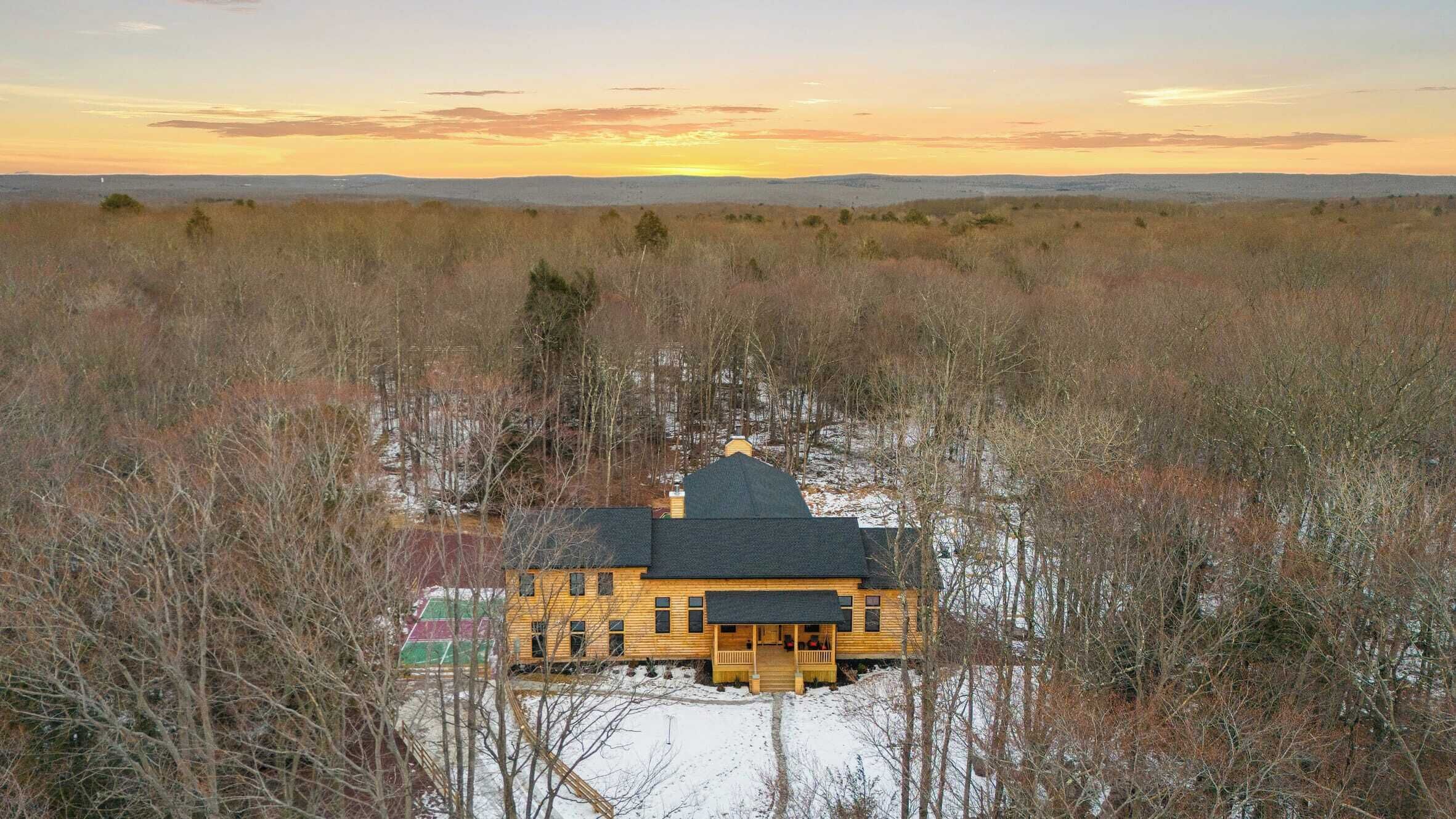 A log cabin with a dark roof, surrounded by a snowy landscape and dense trees.