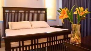 A bedroom with a wooden bed, white bedding, and a vase with flowers on a nightstand.
