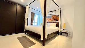 A four-poster canopy bed with a headboard mural, a bedside table with a lamp, and a large window with curtains.