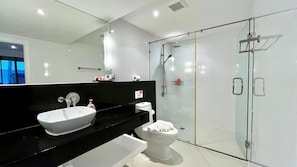 A modern bathroom with a large mirror, a white sink, a toilet, and a glass-enclosed shower area.