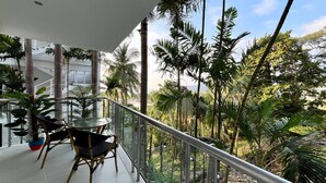 A balcony with a glass railing overlooking a lush garden with tall palm trees and other greenery.