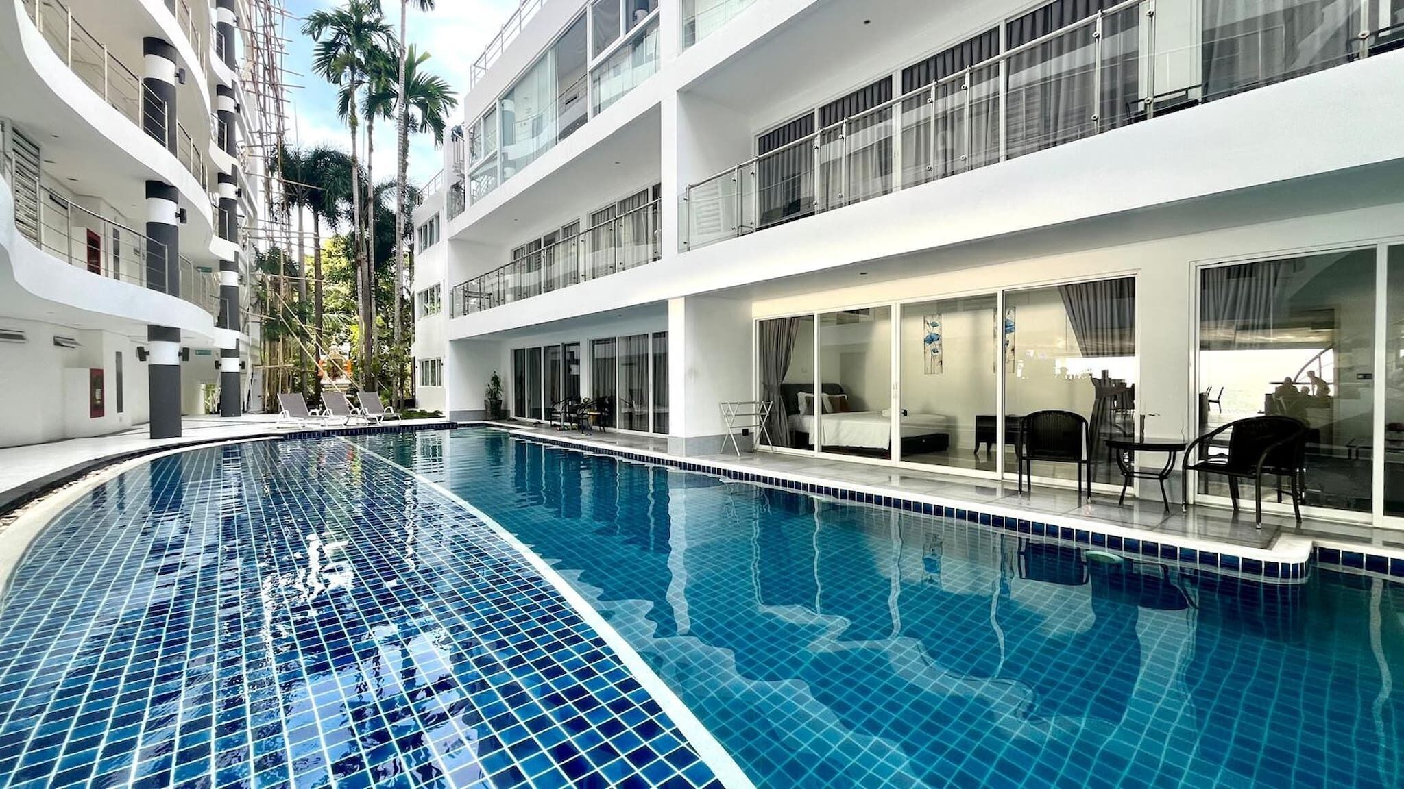 A modern hotel with a large indoor swimming pool, multiple balconies, and a view of palm trees.
