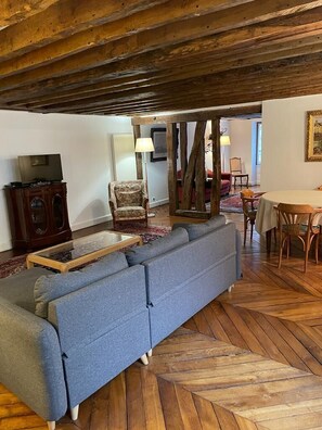 A living room with a blue sofa, wooden floor, and a dining area with a table and chairs.