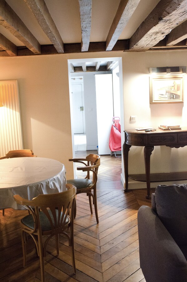 A room with a round table, wooden chairs, a sofa, and a wooden floor. - Beautiful, family-ready space in the historical heart of Paris! (Paris)