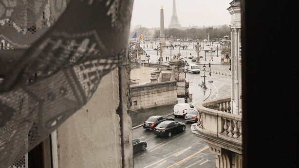 Vista desde una ventana sobre una calle concurrida, con coches, un monumento y edificios.