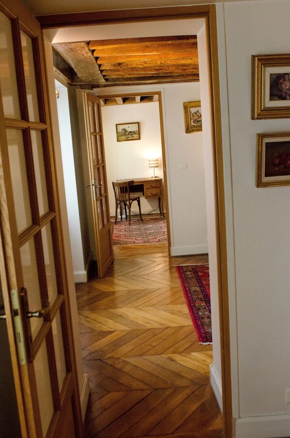 A hallway with wooden flooring, a dining area with a table and chairs, and a red patterned rug.