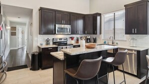 Una cocina moderna con armarios oscuros, una isla central con taburetes, electrodomésticos de acero inoxidable y un amplio ventanal.
