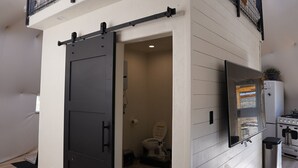Een kleine badkamer met een zwarte schuifdeur, een toilet, een wit wastafeltje en een spiegel.