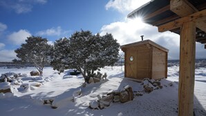 Een houten blokhut met een rond raam, omringd door een met sneeuw bedekte grond en bomen.
