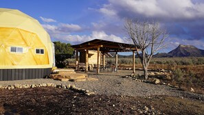 Une structure en forme de dôme géodésique jaune, dotée d’un pavillon en bois et d’un espace extérieur aménagé pour s’asseoir.