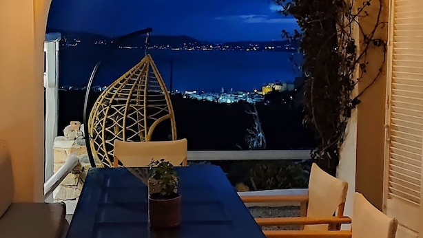A dining area with a table and chairs, a potted plant, and a view of the city at night. - Zephyrus Sunset House  (Naxos)