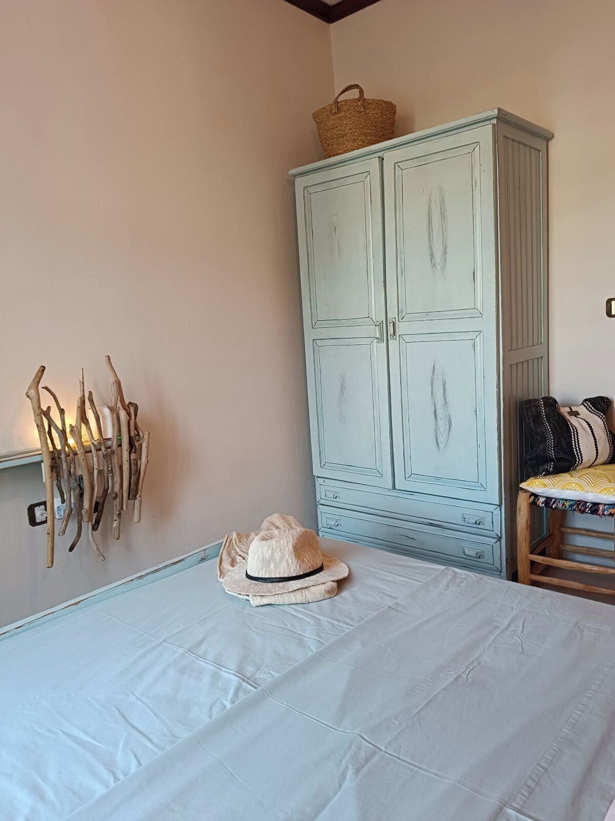 A bedroom with a bed, a wardrobe, a wall-mounted hat rack, and a chair.