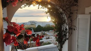 A cozy outdoor seating area with a table and chairs, surrounded by a decorative arch of red flowers and climbing plants. - Zephyrus Sunset House  (Naxos)