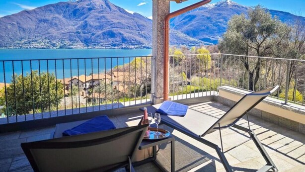 A balcony with a view of a lake and mountains. There are two lounge chairs and a table with a bottle and glass. - VILLA DEI VENTI-BREVA by Curti rentals (Calozzo)