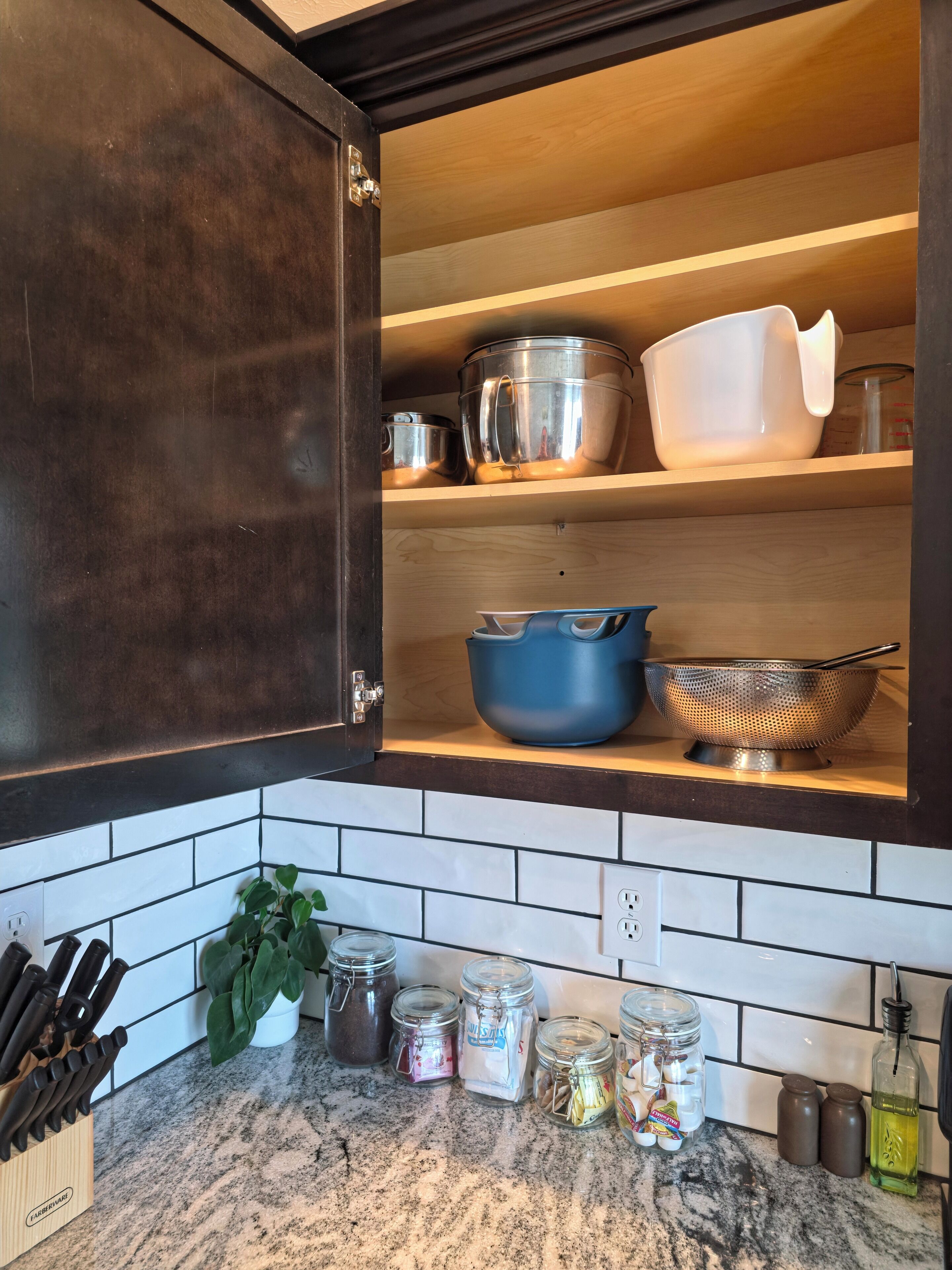 Una cocina con armarios de madera oscura, encimera de mármol y diferentes utensilios y recipientes de cocina.
