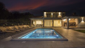 Ein zweistöckiges Haus mit Swimmingpool, Sitzgelegenheiten im Freien und einer Terrassenfläche.