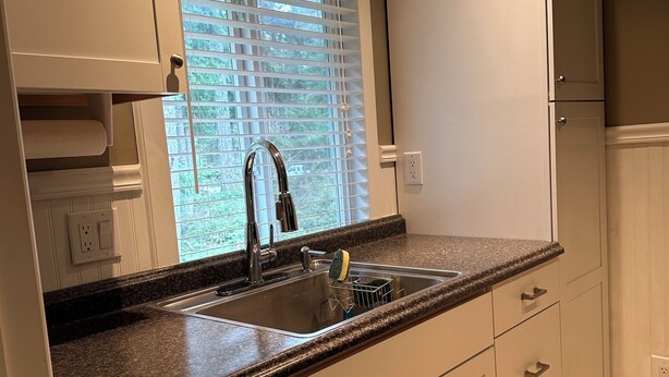Cocina con encimera de granito, armarios blancos, pileta de acero inoxidable y ventana con persianas.