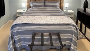 Un dormitorio con cabecera de madera, cama con ropa de cama a rayas, dos mesitas de noche con lámparas y un ventilador de techo.