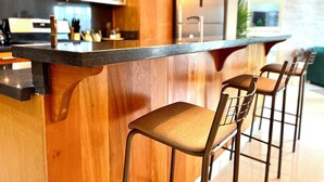 Une cuisine moderne avec des meubles en bois, un réfrigérateur en acier inoxydable et un coin bar équipé de tabourets.