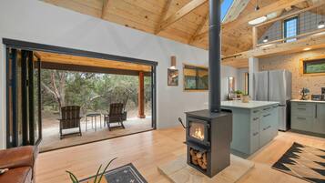 A modern interior with a large wooden ceiling, a central fireplace, a kitchen area, and a seating area with a view of the outdoors.