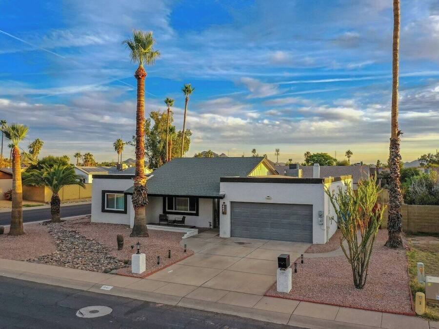 A modern two-story house with a garage, surrounded by palm trees and a clear sky.