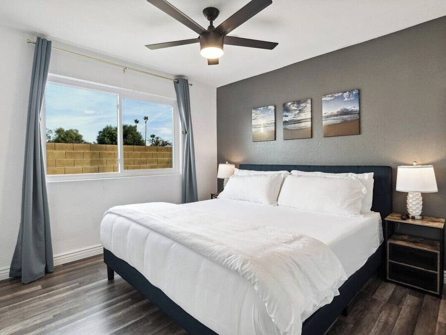 A bedroom with a bed, a ceiling fan, a nightstand with a lamp, and a window with curtains.