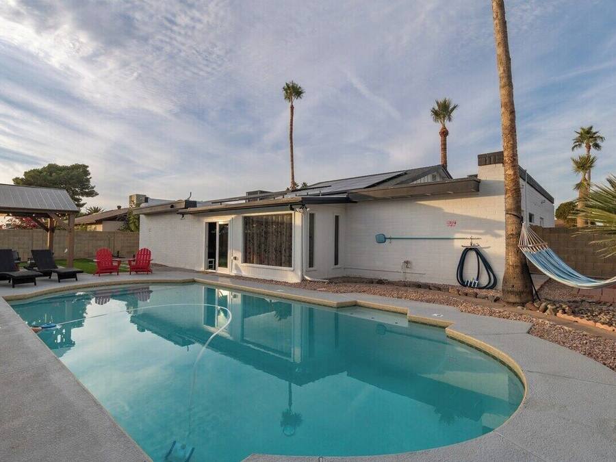 A swimming pool with lounge chairs, palm trees, and a modern house with a white exterior.