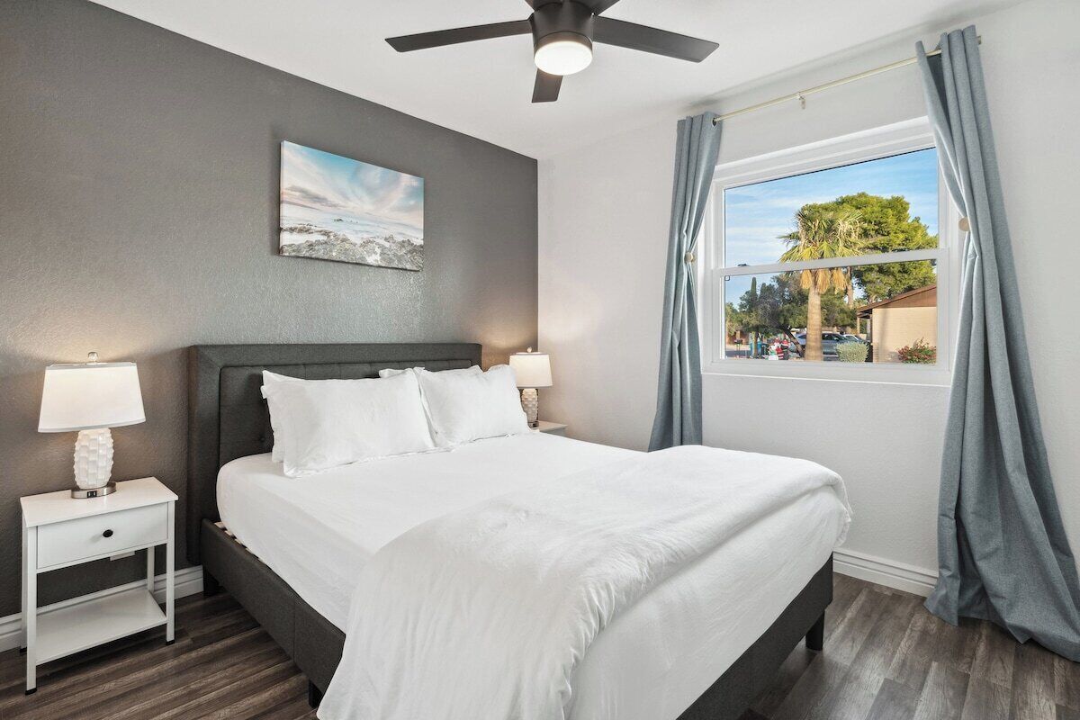 A neatly arranged bedroom with a bed, bedside tables, a ceiling fan, and a window with curtains.