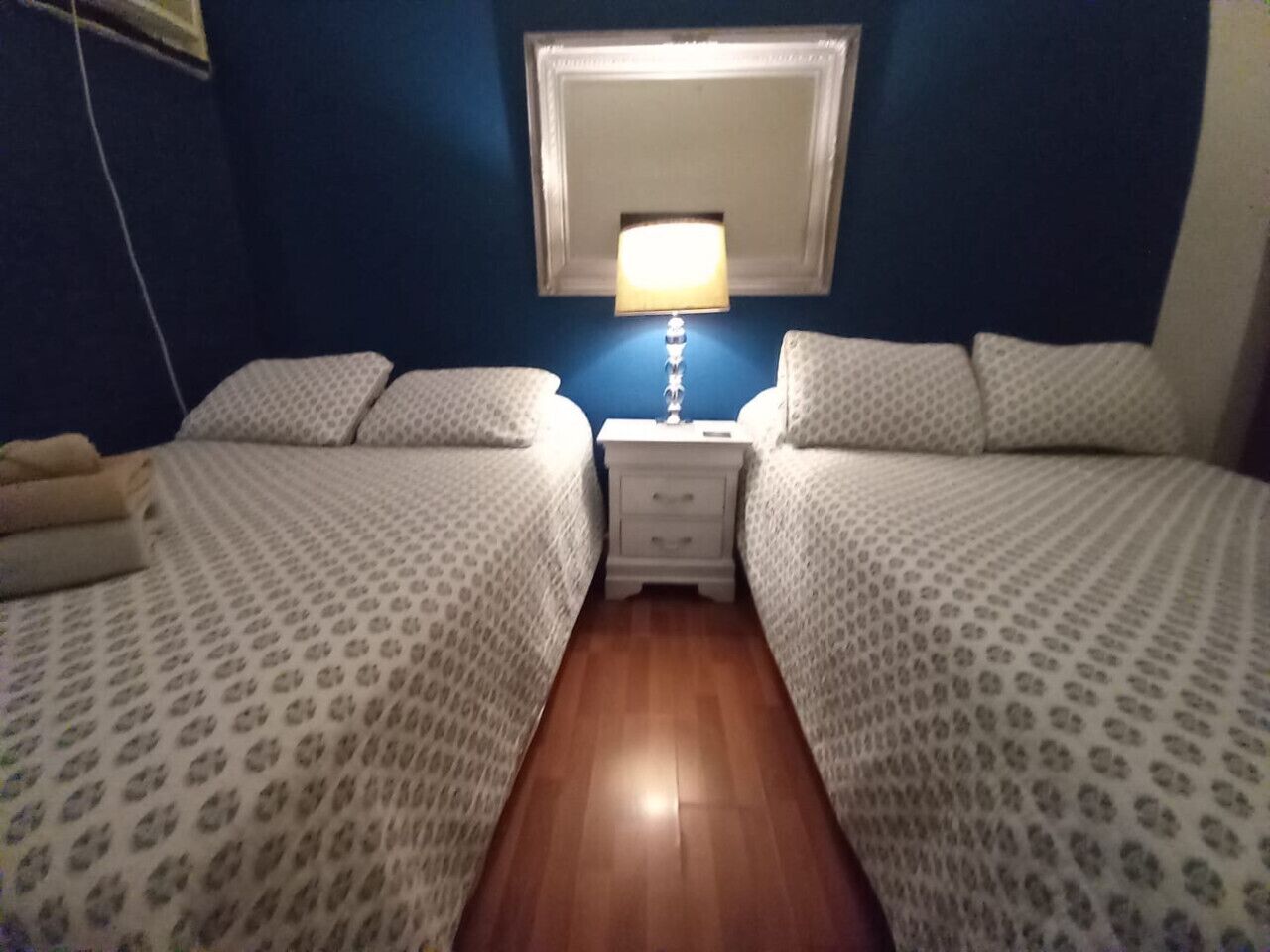 Een kamer met twee bedden, een nachtkastje met een lamp en een spiegel aan de muur.