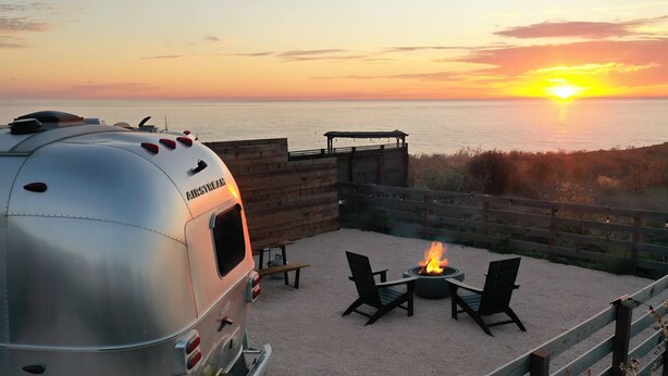 A camper with a fire pit and chairs on a sandy area overlooking the ocean at sunset. - Cool California Coast Airstream (Half Moon Bay)