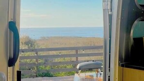 A view through a window with a wooden fence and a body of water in the distance. - Cool California Coast Airstream (Half Moon Bay)