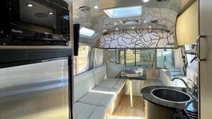 A compact kitchen with a microwave, a sink, and a window providing natural light. - Cool California Coast Airstream (Half Moon Bay)